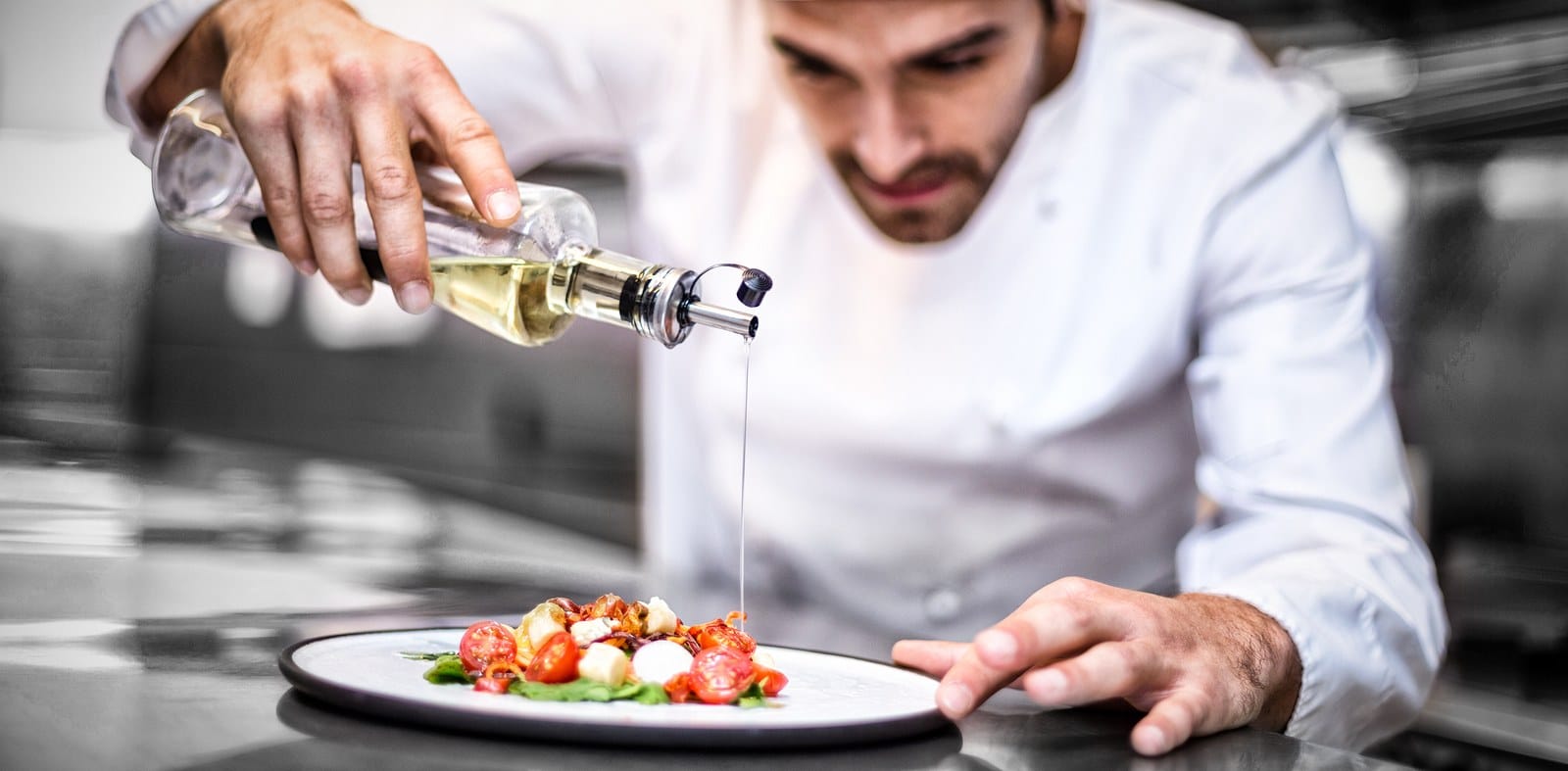 A chef carefully pouring oil on a salad